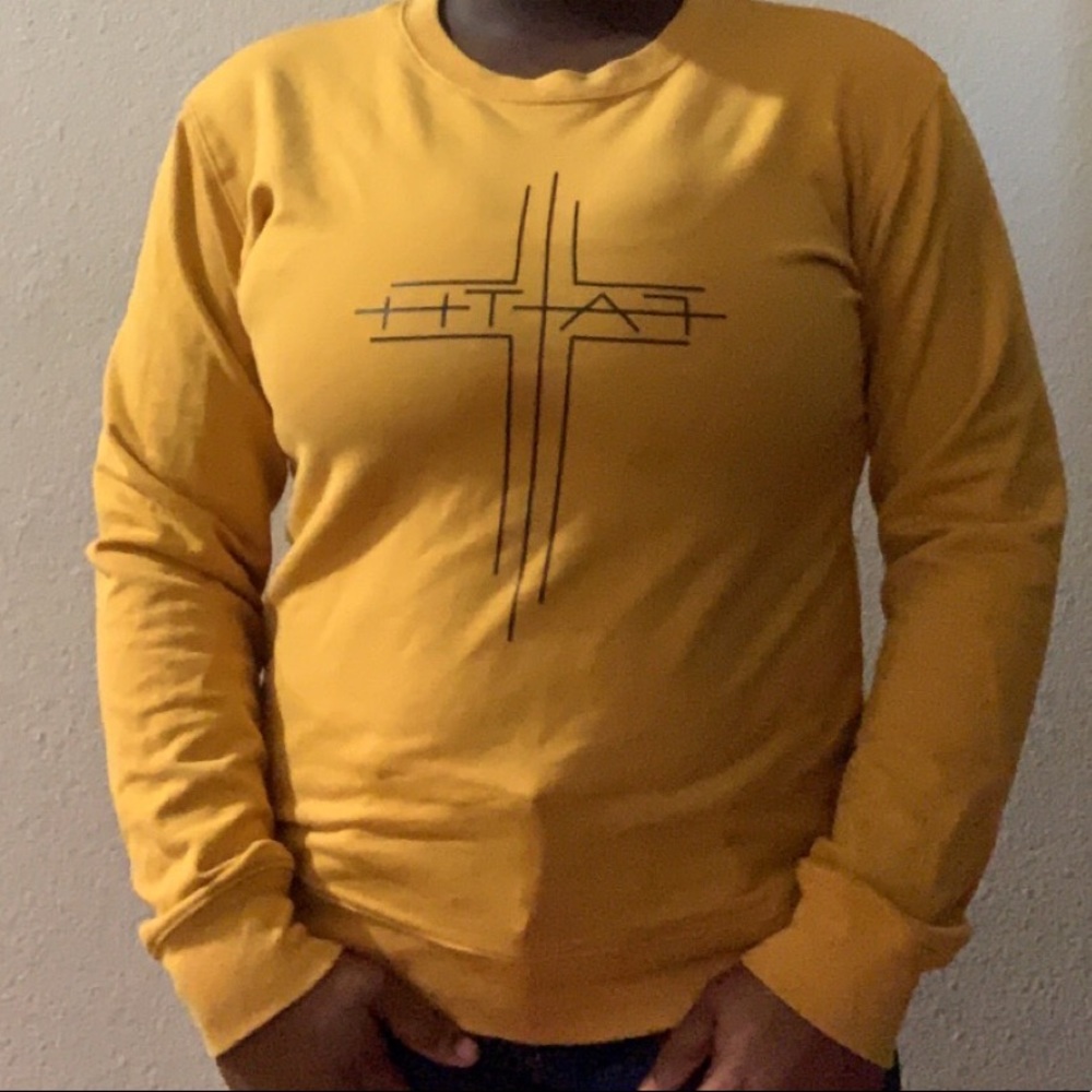 A yellow gold sweater. With black faith writing on it. Long sleeves.